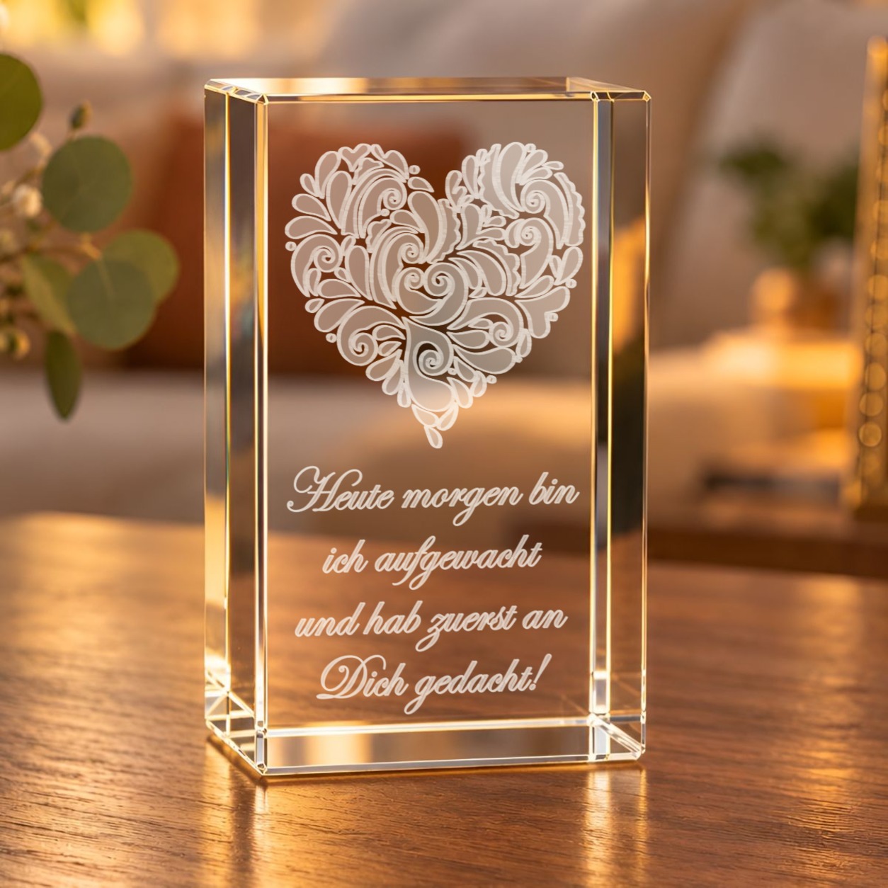 Glaskristall Herz mit Ornamenten und Liebesspruch in 3D-Laserinnengravur auf einem Holztisch im Wohnzimmer bei warmem Licht