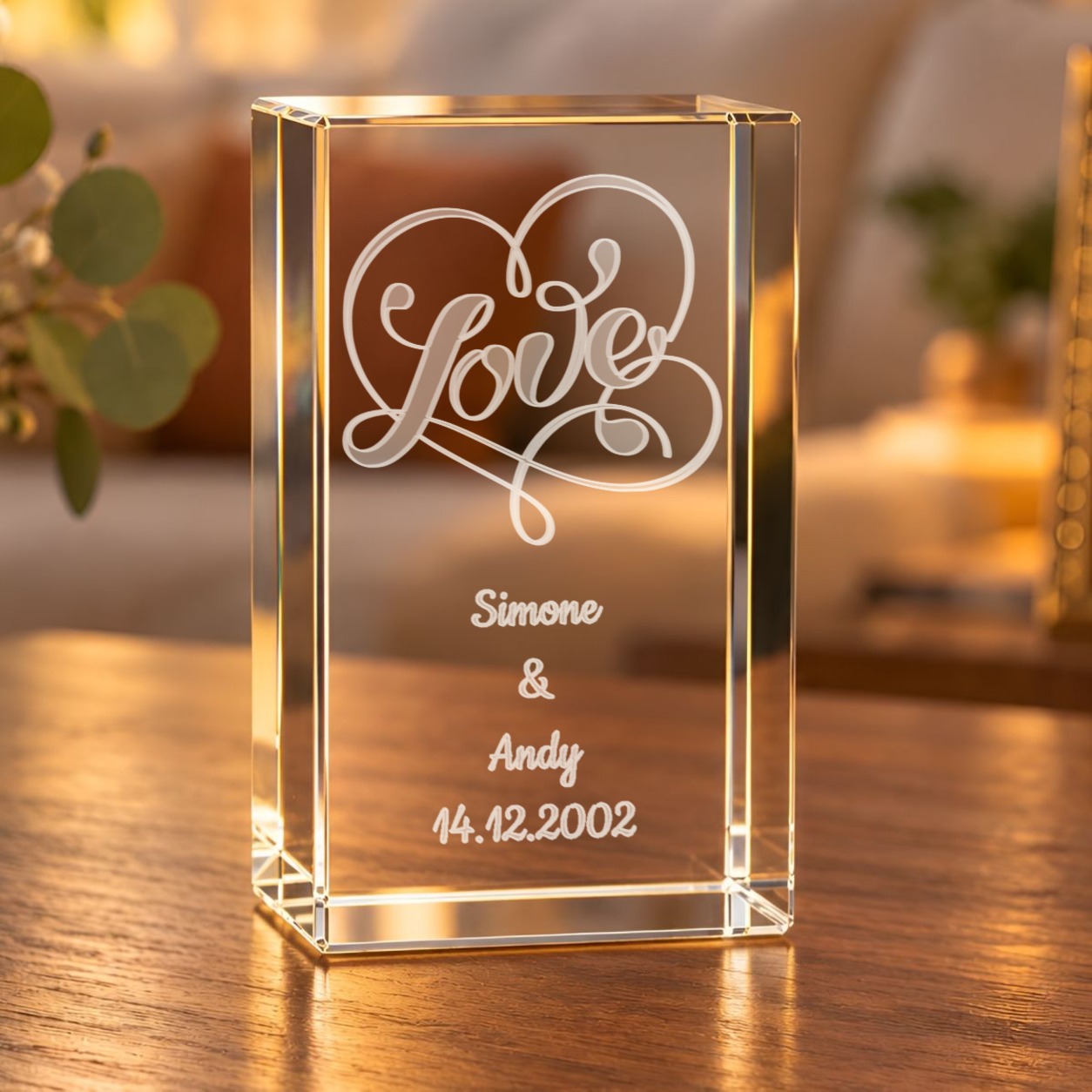 Glaskristall Love mit Wunschtext: Glasquader mit gravuriertem Love-Schriftzug im Herz und zwei Namen mit Datum auf einem Holztisch im Wohnzimmer
