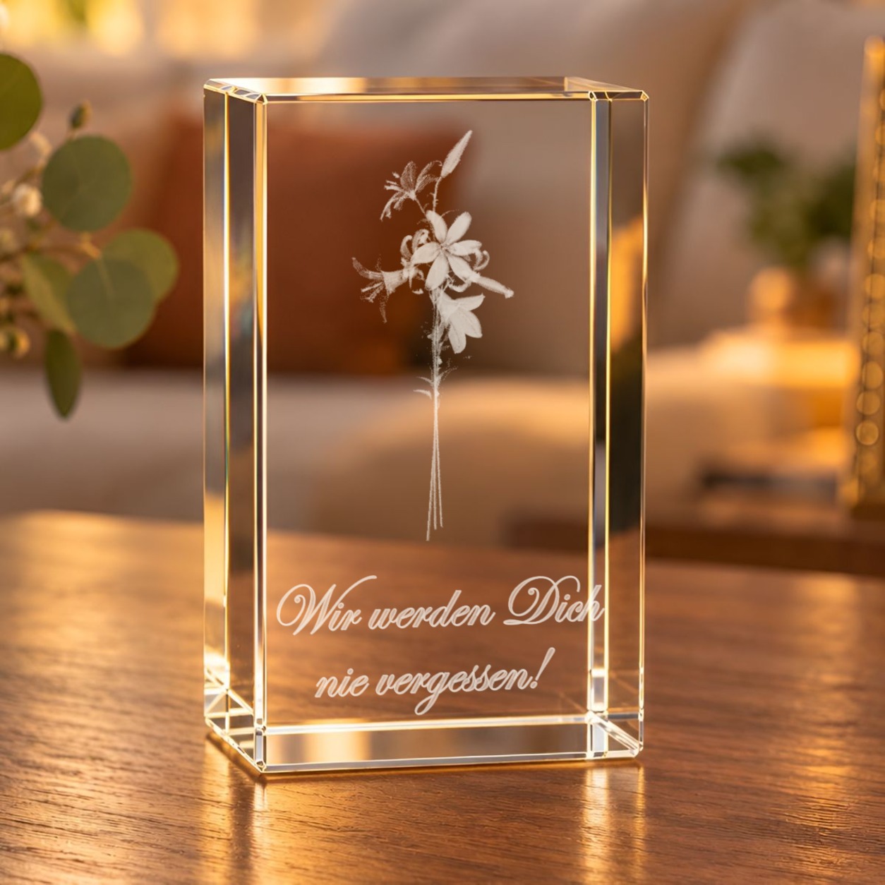 Glaskristall Lilien mit gravierter Schreibschrift „Wir werden Dich nie vergessen!“ auf einem Holztisch im warm beleuchteten Wohnraum