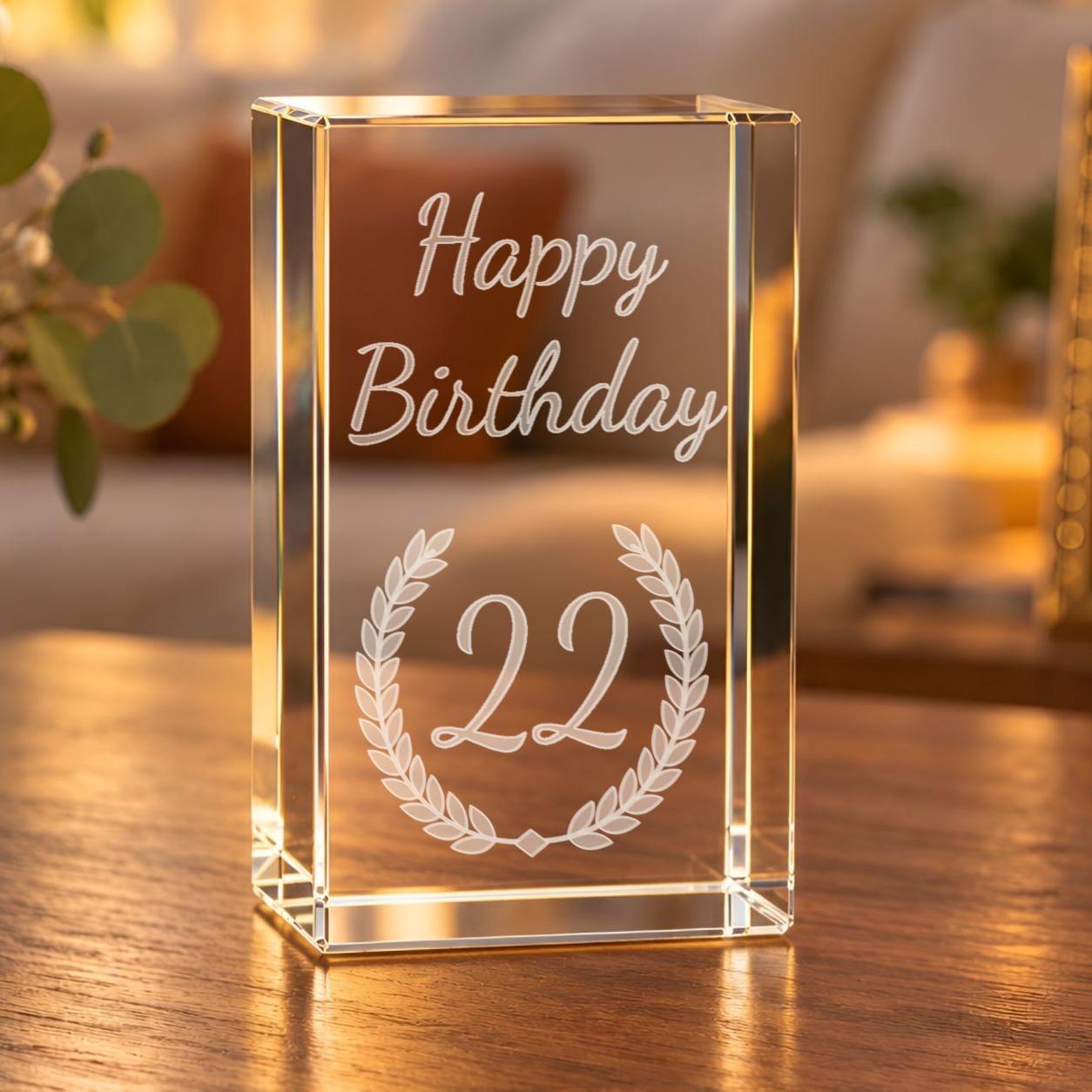 3D-Glaskristall Lorbeerkranz Happy Birthday mit Zahl 22 als Wunschtext, auf einem Holztisch im warm beleuchteten Wohnzimmer