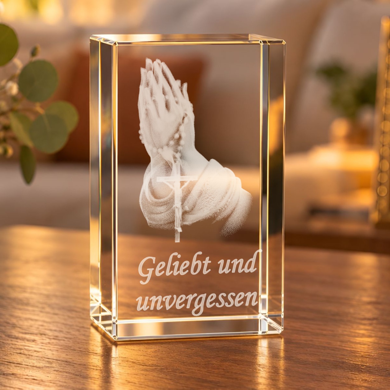 Glaskristall Betende Hände mit Rosenkranz und Schriftzug „Geliebt und unvergessen“ auf einem Holztisch im warm beleuchteten Wohnzimmer