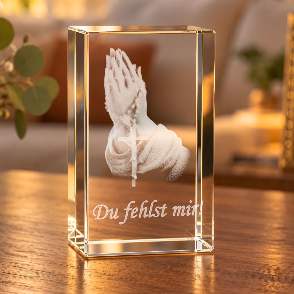 Glaskristall Betende Hände mit Rosenkranz und Schriftzug „Du fehlst mir!“ auf einem Holztisch im Wohnzimmer bei warmem Licht