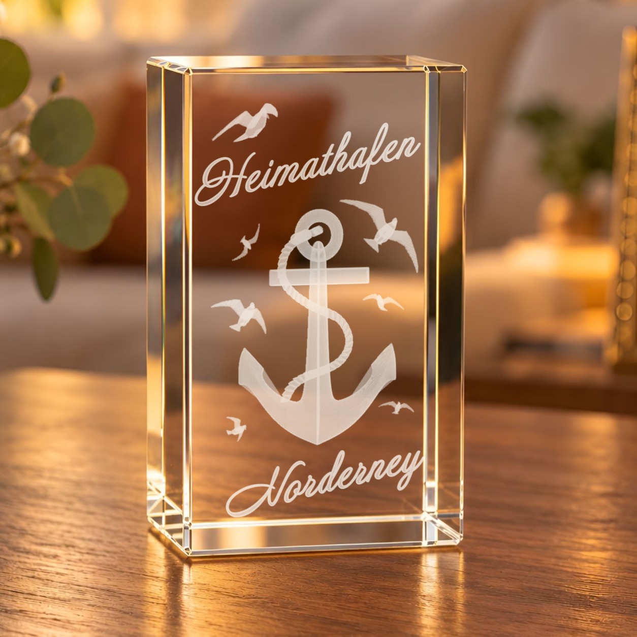 Glaskristall Norderney mit 3D-Gravur von Anker, Möwen und Schriftzug „Heimathafen Norderney“ auf einem Holztisch im Wohnzimmer