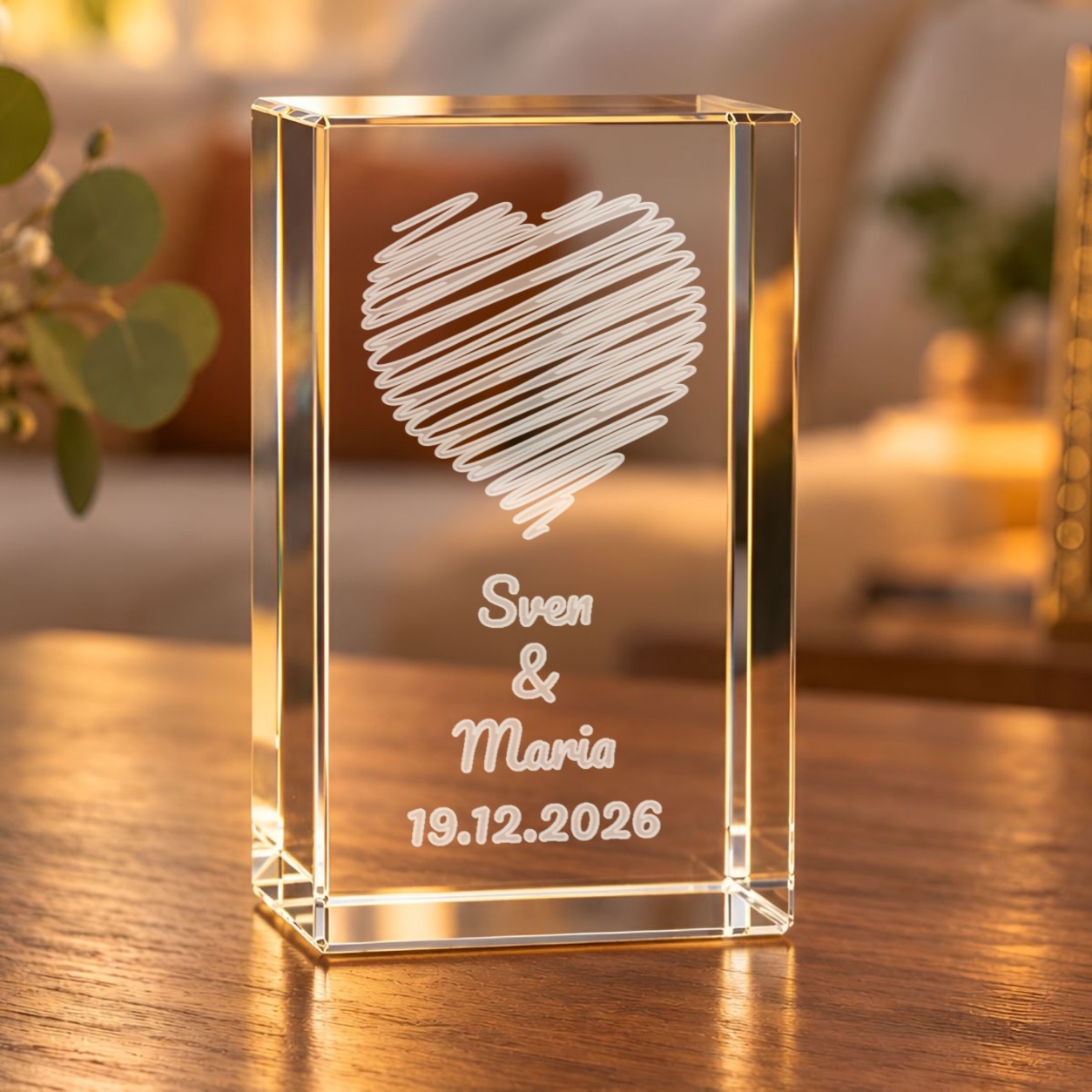 Glaskristall mit Wunschtext und gestreiftem Herz, graviert mit zwei Namen und Datum, auf einem Holztisch im Wohnzimmer
